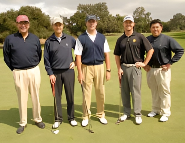 Five men posing on a golf course with clubs.
