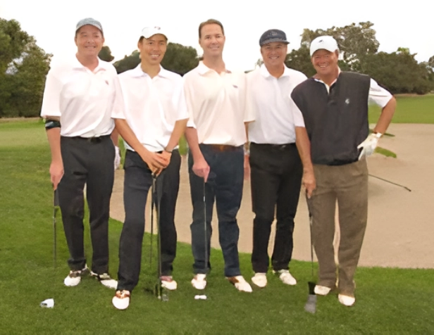 Five men standing on a golf course holding clubs.