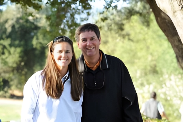A smiling couple outdoors with trees in the background.