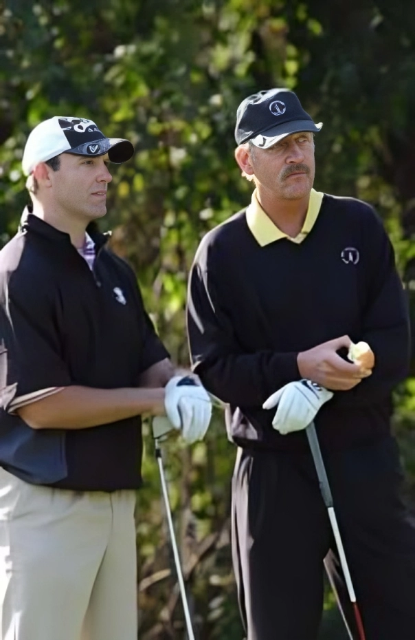 Two men in golf attire holding clubs on a sunny day.