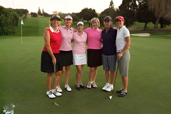 Six women golfers posing together on a golf course.