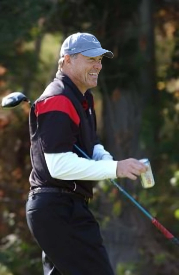A man smiling while holding a golf club and a drink can.