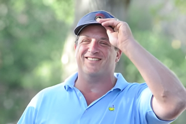 A smiling man in a blue polo shirt and baseball cap outdoors.