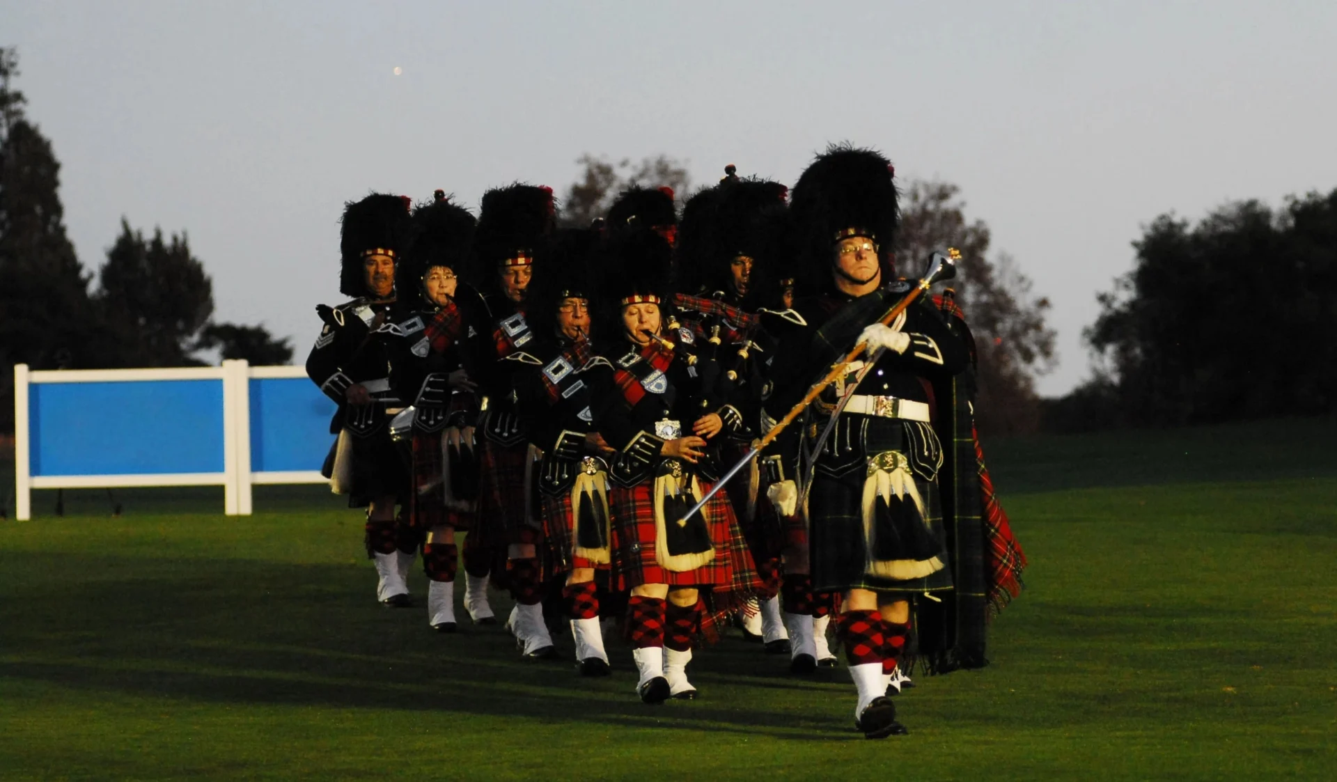 A group of bagpipers in traditional Scottish attire marching outdoors.