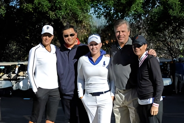 Group of five adults posing outdoors on a sunny day.