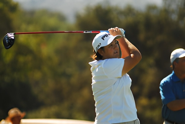 A young golfer in a white shirt swinging a golf club outdoors.