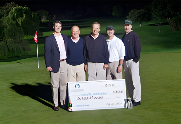 Five men holding a large check on a golf course at night.