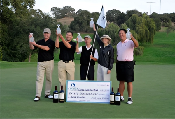 A group of six men celebrating with a large check and champagne bottles on a golf course.