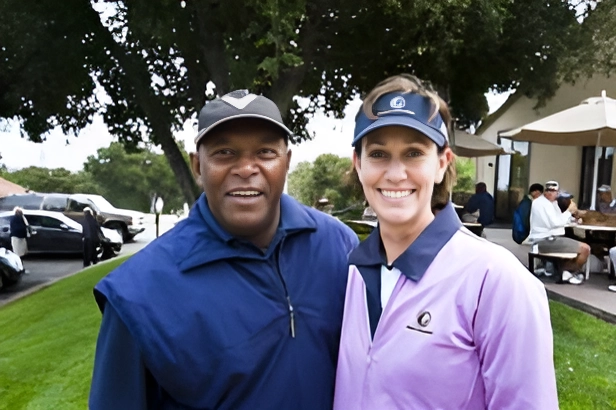 Two people smiling outdoors with trees in the background.