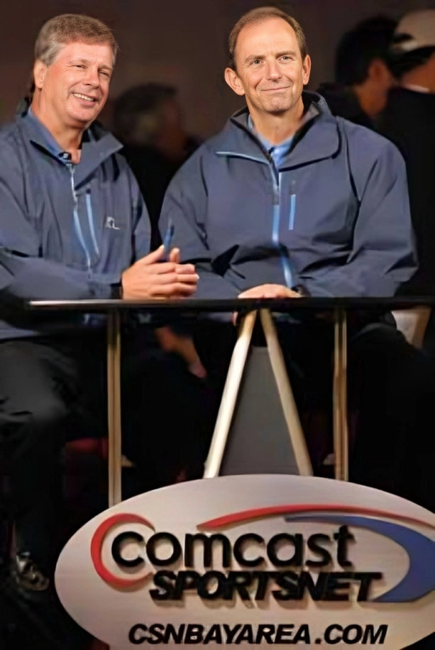 Two men in blue jackets sitting at a Comcast desk.