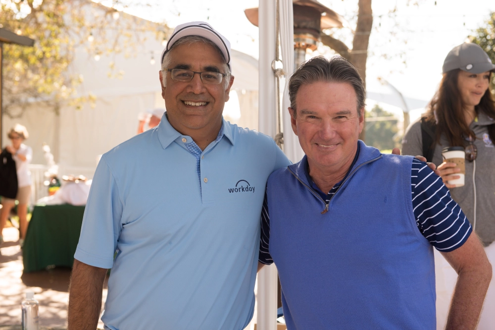 Two smiling men posing outdoors on a sunny day.