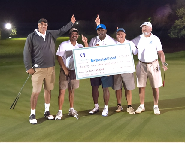 Golfers posing with a large check on a golf course at night.