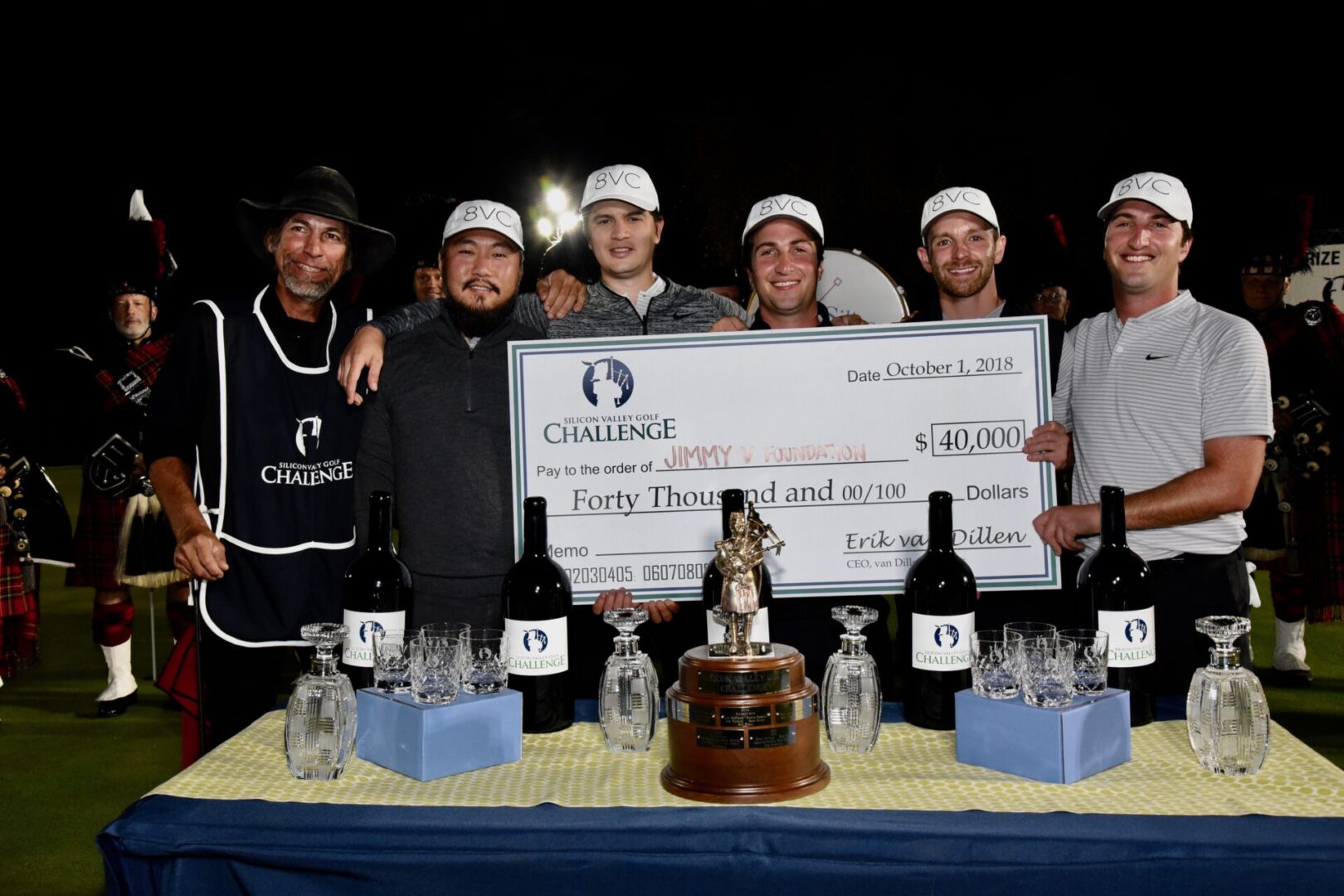 A group of men posing with a large check and bottles on a table.