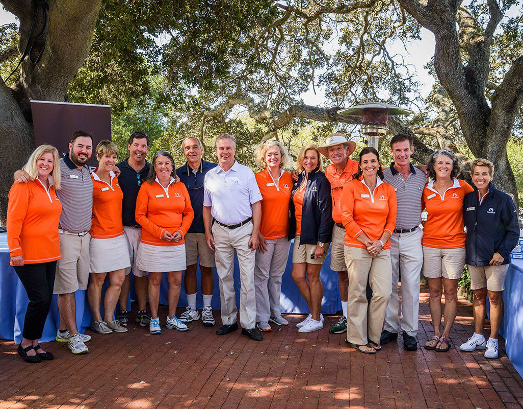 A group photo of people in matching orange shirts and casual attire outdoors.